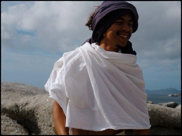 Matthew Gabriel smiling outdoors by the ocean, wrapped in a white cloth